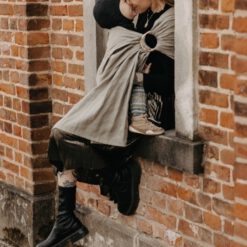 tragetuch aus leinen - Frau sitzt in Fensterbank mit Baby im Tragetuch aus Leinenstoff