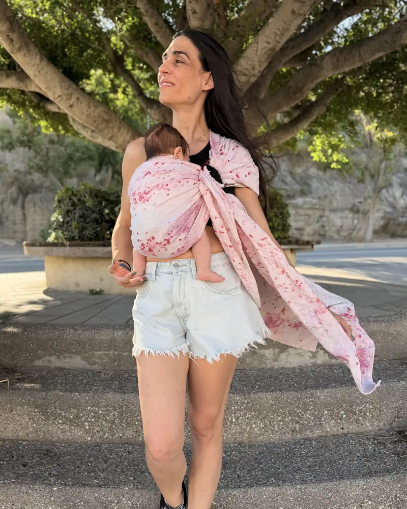 Frau trägt ihr Baby im Mariblum Babytragetuch Kiss from a Rose während eines Spaziergangs.