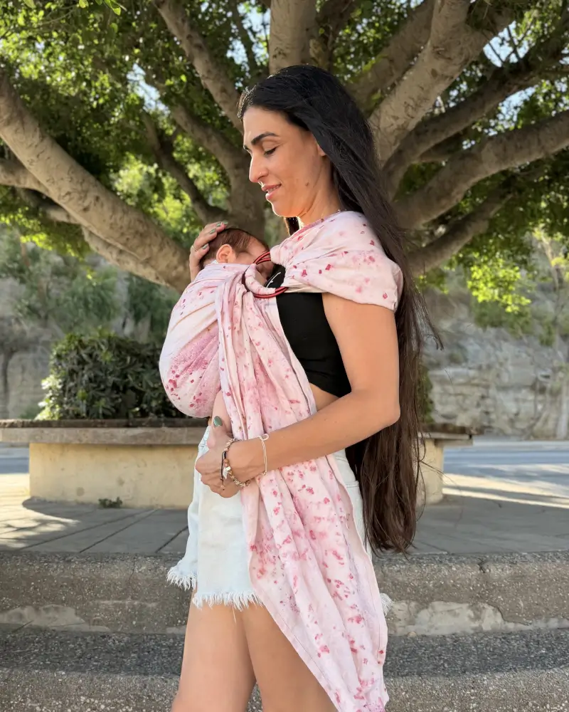Mutter hält den Kopf ihres Babys im Mariblum Ringsling Kiss from a Rose mit rosafarbenem Blütenmuster.