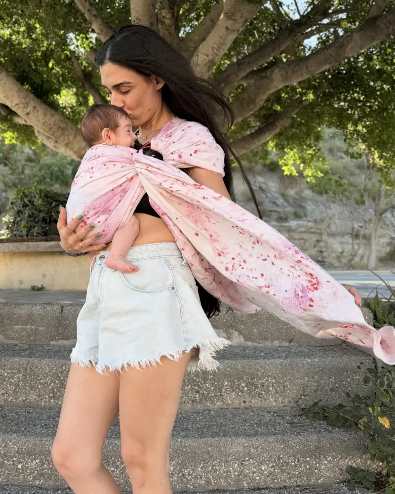 Mutter küsst ihr Baby im Mariblum Ringsling Kiss from a Rose mit rosafarbenem Blumenmuster.