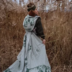 Femme porte son bébé dans l'herbe de roseau d'automne sur le dos. La longue écharpe vert clair à motif éléphant tombe avec élégance comme une robe.