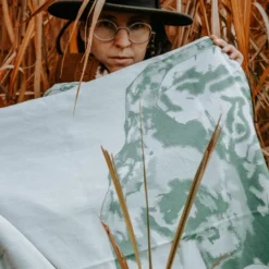 La femme se tient dans le roseau haut et tient le tissu de l'écharpe verte pour bébé pour présenter le motif d'éléphant tissé en détail.