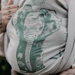 Close-up of a tied baby sling in green and white. A detailed elephant head and a small mandala on the baby's back can be seen.