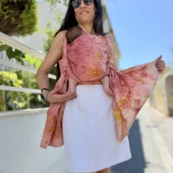 Modische Mutter trägt ihr Baby im rosa mariblum Tragetuch aus Hanf als praktische Alternative zum Kinderwagen.